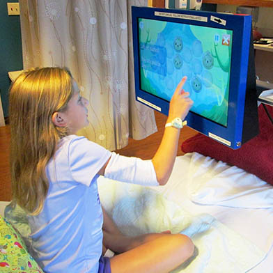 A young girl playing games on the Touch2Play Max while sitting in a hospital bed.