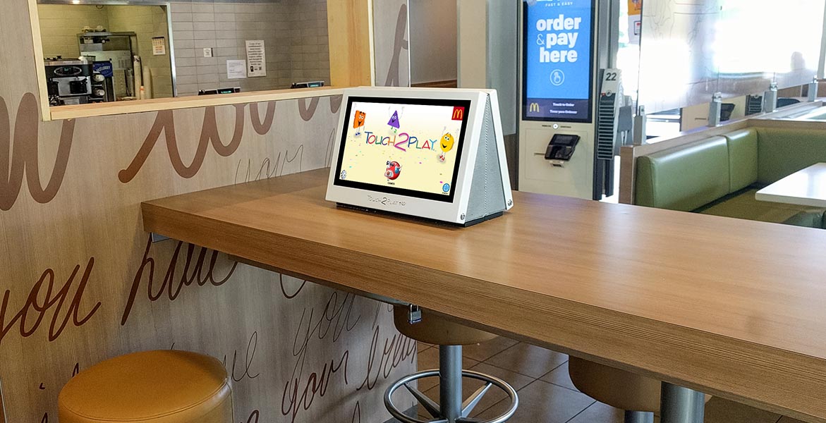 Touch2Play Pro interactive touchscreen game cabinets mounted back-to-back in a McDonald's restaurant