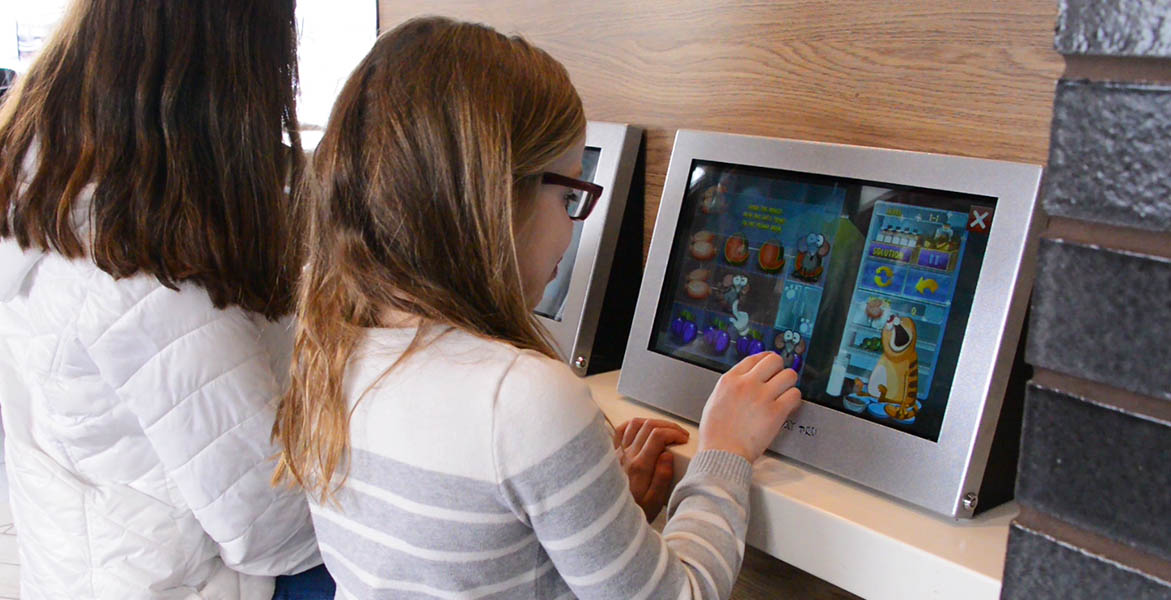Kids playing on Kidzpace Touch2Play Pro interactive game kiosk. Great for any area where customer or patients are waiting for their appointment.
