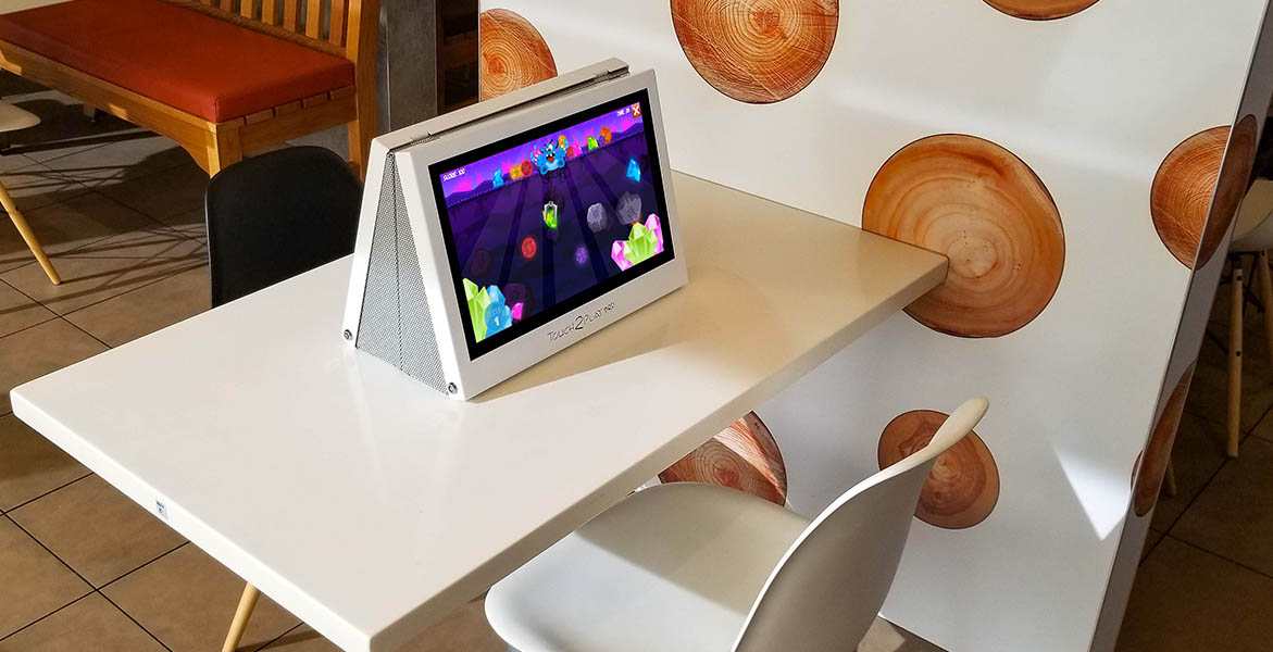 Touch2Play Pro interactive touchscreen game cabinets mounted back-to-back in a McDonald's restaurant